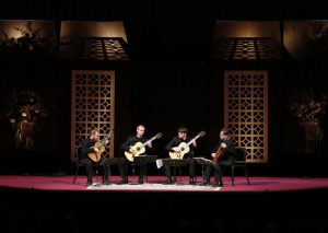 Georgia Guitar quartet on a dark stage with bright lights shining on the musicians